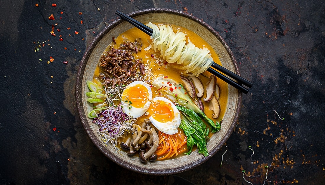 Miska asijské polévky ramen s bezlepkovými nudlemi, vejcem naměkko, masem, houbami a zeleninou na tmavém pozadí.