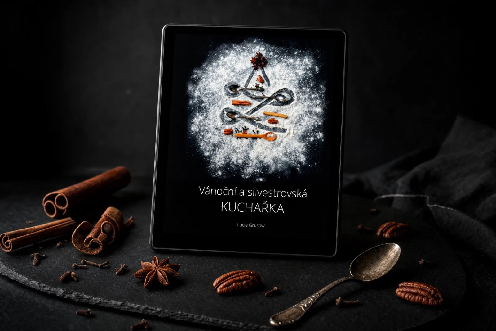 Vánoční a silvestrovská kuchařka na tabletu v tmavém studiu, kolem skořicové kůry, hvězdičky badyánu a pekanové ořechy