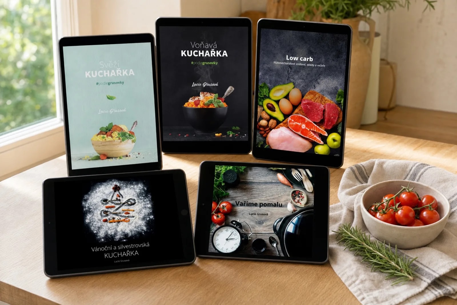 Pět tabletů s obálkami e-kuchařek na světlém kuchyňském stole u okna