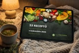 E-kniha 53 receptů z kalendáře 2024 na tabletu položeném na pletené dece na pohovce ve večerním světle stolní lampy, vedle hrnek bylinkového čaje na dřevěném podtácku