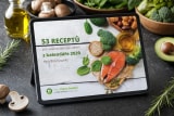 E-kniha 53 receptů z kalendáře 2020 na tabletu opřeném na tmavé břidlicové desce, kolem žampiony, brokolice, půlka avokáda, rozmarýn a láhev olivového oleje